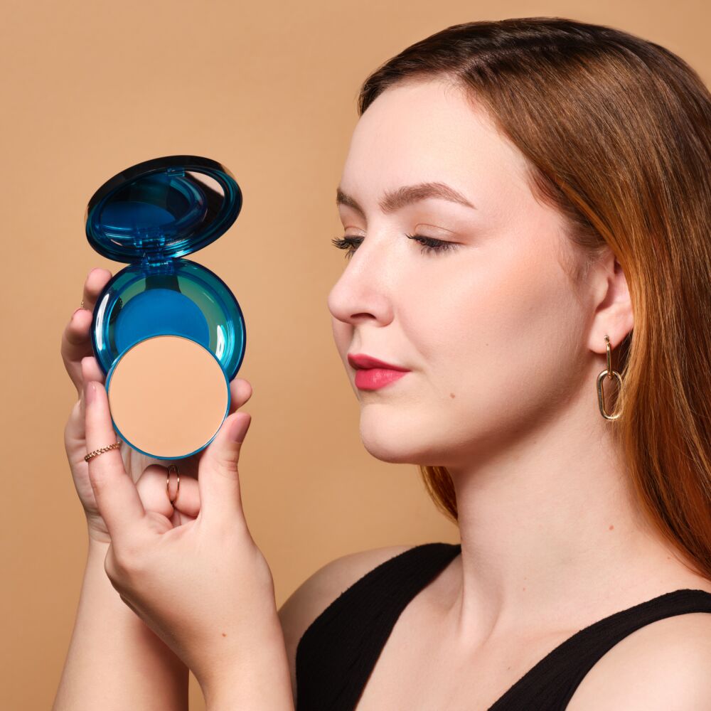 Junge Frau hält das Sun Protection Powder Foundation mit LSF 50 in ihren Händen und zeigt die Nachfüllbarkeitsfunktion.