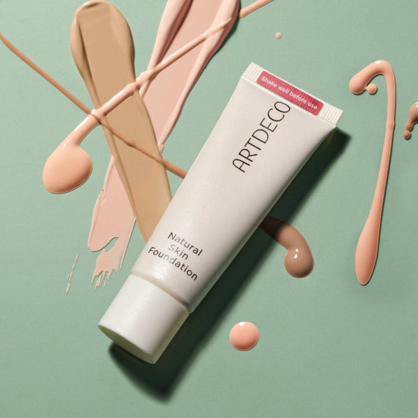 Die Natural Skin Foundation auf grünem Hintergrund mit Swatches verschiedener Farben der Foundation.  
