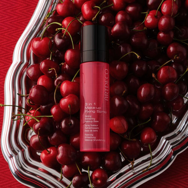 3 In 1 Make-up Fixing Spray platziert auf roten Kirschen, passend zum neuen roten Packaging des Produkts.