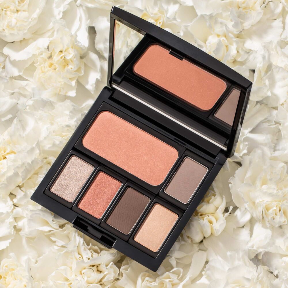 Produktbild einer Lidschatten Palette mit Aprikos und Braun-Tönen. Die Palette liegt auf weißen Blumen.