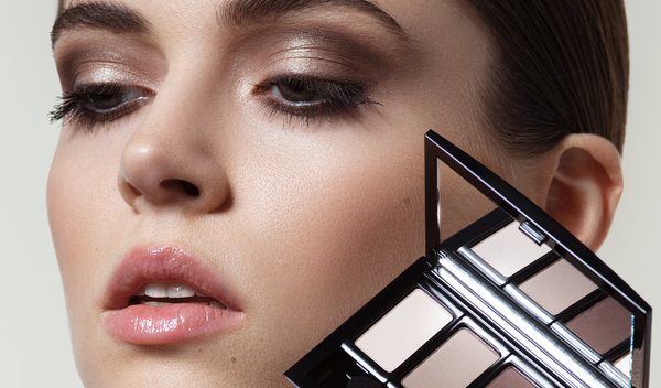 Frau mit geschminkten Augen hält Beauty Box mit Lidschatten in der Hand
